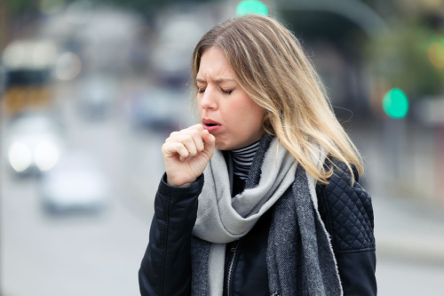 Donna per strada tossisce tenendosi la mano chiusa a pugno davanti alla bocca